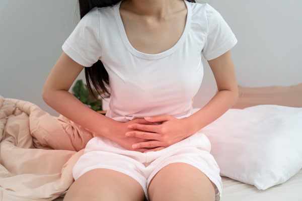 Woman experiencing abdominal pain and cramping, holding her stomach in discomfort while seated.