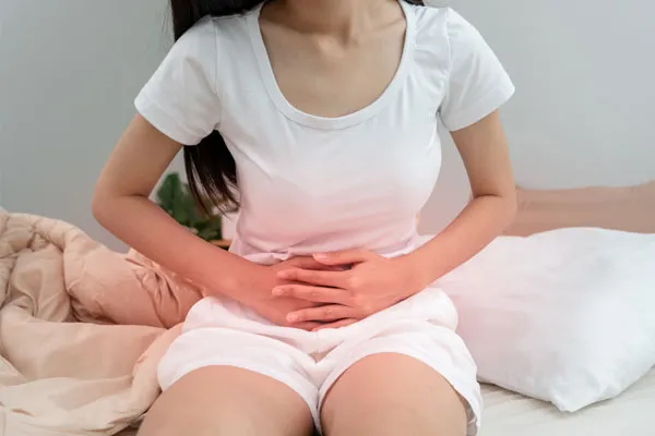 Woman experiencing abdominal pain and cramping, holding her stomach in discomfort while seated.