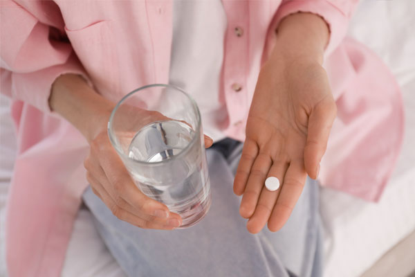 Young woman holding an abortion pill in one hand and a glass of water in the other.